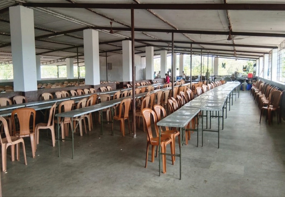 Large hostel dining hall with long tables and rows of plastic chairs arranged for students